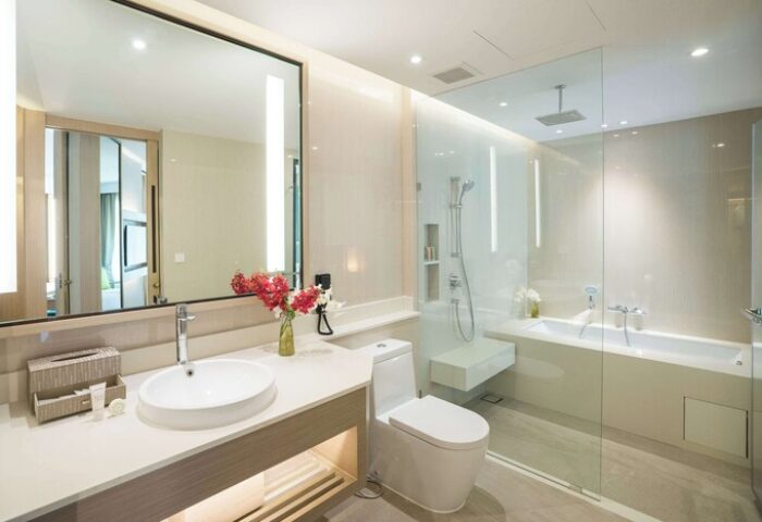 Avani+ Hua Hin Resort gay-friendly hotel bathroom. Modern design with a large mirror, white sink, toilet, and glass-enclosed shower/tub.