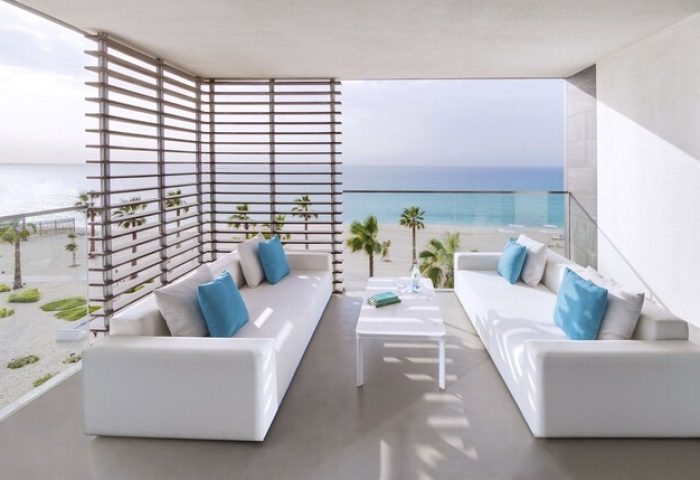 Nikki Beach Resort & Spa Dubai gay-friendly hotel balcony view. White sofas, blue pillows, beach, and ocean. Luxury travel for gay men.