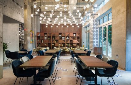 Hotel Indigo Miami Brickell gay-friendly hotel dining area. Tables with blue chairs, modern lighting, and geometric shelving. Stylish, welcoming space.