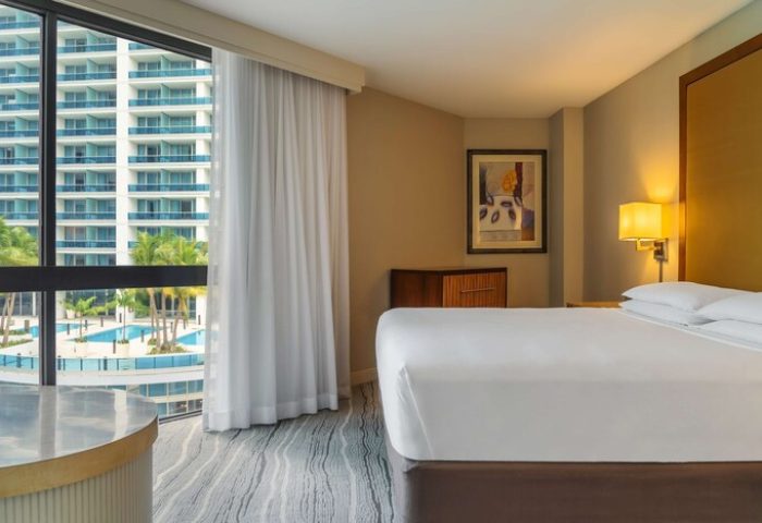 Hyatt Regency Miami gay-friendly hotel room; view of pool, palm trees, and building. Modern decor, white linens, and natural light. Ideal gay travel.
