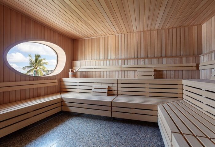 Sauna at The Standard Miami, a gay-friendly hotel. Wood benches, oval window with palm tree view. Ideal for relaxation and wellness.