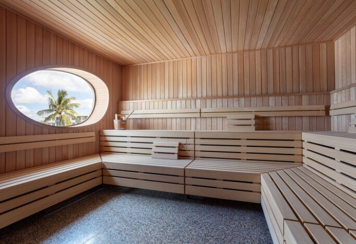 Sauna at The Standard Miami, a gay-friendly hotel. Wood benches, oval window with palm tree view. Ideal for relaxation and wellness.