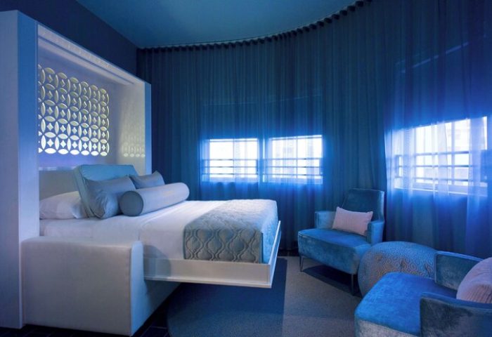 Dream South Beach hotel room in blue tones. Gay-friendly hotel with bed, chairs, and windows. Modern design for gay men's travel.