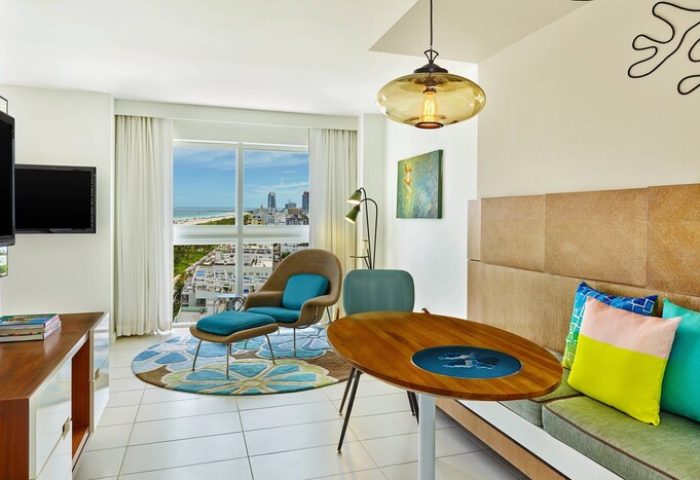 Royal Palm South Beach Miami suite. Gay-friendly hotel room with stylish decor, ocean view, lounge chair, and dining area. Modern design.