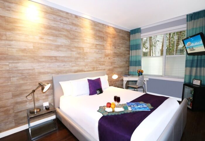 Hotel Shelley gay-friendly room: Queen bed with tray of fruit, wine, and Miami magazine. Desk, TV, and mini-fridge. Wood accent wall.