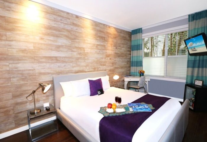 Hotel Shelley gay-friendly room: Queen bed with tray of fruit, wine, and Miami magazine. Desk, TV, and mini-fridge. Wood accent wall.