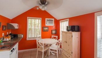 Wicker Guesthouse gay-friendly hotel room. Orange walls, dining table, kitchenette, and ceiling fan. Gay travel lodging option.