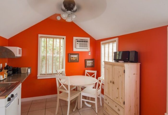 Wicker Guesthouse gay-friendly hotel room. Orange walls, dining table, kitchenette, and ceiling fan. Gay travel lodging option.