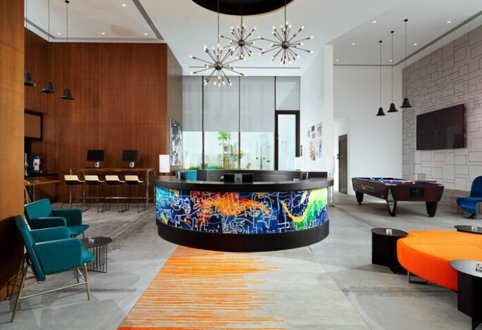 Aloft Me'aisam Dubai's gay-friendly hotel lobby. Modern design with a colorful reception desk, pool table, lounge area, and computer stations.