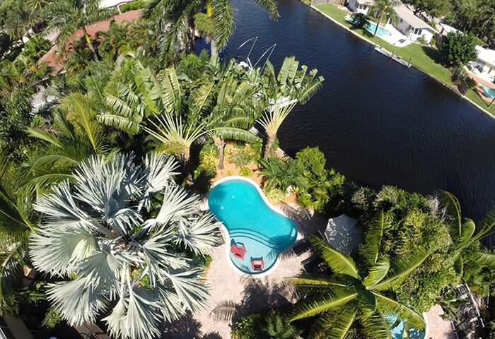 Aerial view of The Cabanas Guesthouse & Spa, a gay men's resort. Lush tropical landscaping surrounds a kidney shaped pool near a canal.