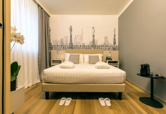 43 Station Hotel room. Gay-friendly hotel with a bed, slippers, and Milan skyline art. Comfortable stay for gay travelers. #gaytravel #Milan #hotel