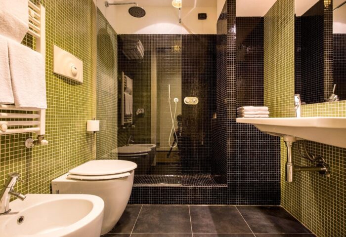 Bathroom at 43 Station Hotel, a gay-friendly hotel. Features a toilet, bidet, shower, and sink with green and black tiles. Modern design.