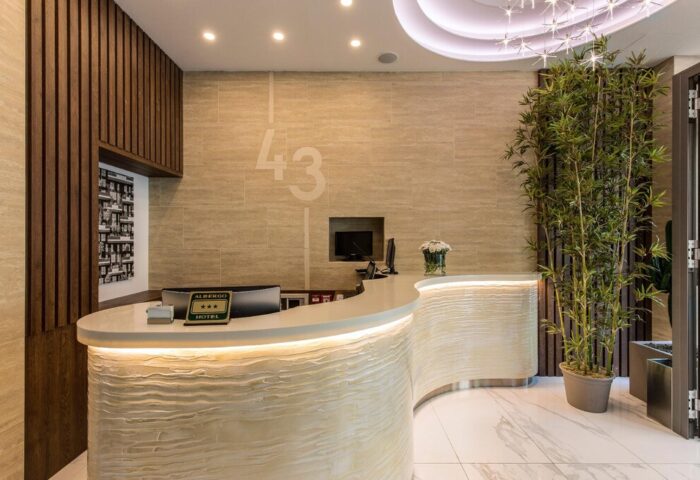Lobby of 43 Station Hotel, a gay-friendly hotel. Modern curved reception desk with LED lighting, bamboo plant, and stylish decor. Gay travel.