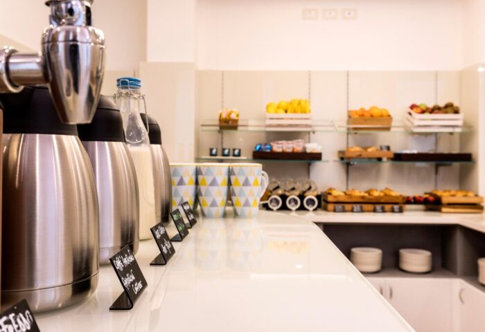 Breakfast buffet at 43 Station Hotel, a gay-friendly hotel. Coffee, milk dispensers, fruit, pastries, and mugs are available for guests.