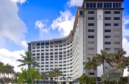 Sonesta Fort Lauderdale Beach, a gay-friendly hotel. Exterior view of the hotel with palm trees and blue sky. Modern architecture.