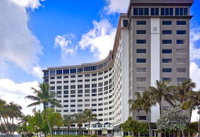 Sonesta Fort Lauderdale Beach, a gay-friendly hotel. Exterior view of the hotel with palm trees and blue sky. Modern architecture.
