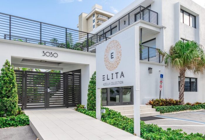 Elita Hotel, a gay-friendly hotel. Modern white building with Elita sign, palm tree, and gated entrance. Ideal for gay men's travel.
