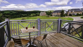 Crieff Hydro gay-friendly hotel balcony view. Drinks on table, chairs, scenic hills, and Scottish countryside. Ideal travel for gay men's vacation.
