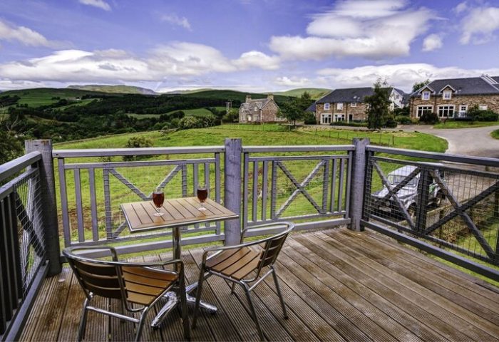 Crieff Hydro gay-friendly hotel balcony view. Drinks on table, chairs, scenic hills, and Scottish countryside. Ideal travel for gay men's vacation.
