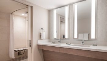 Sheraton Waikiki Beach Resort gay-friendly hotel bathroom. Accessible shower with seat, double sink vanity, and illuminated mirrors. Modern design.