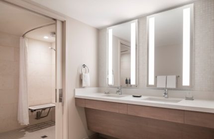 Sheraton Waikiki Beach Resort gay-friendly hotel bathroom. Accessible shower with seat, double sink vanity, and illuminated mirrors. Modern design.