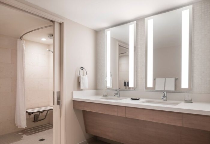 Sheraton Waikiki Beach Resort gay-friendly hotel bathroom. Accessible shower with seat, double sink vanity, and illuminated mirrors. Modern design.