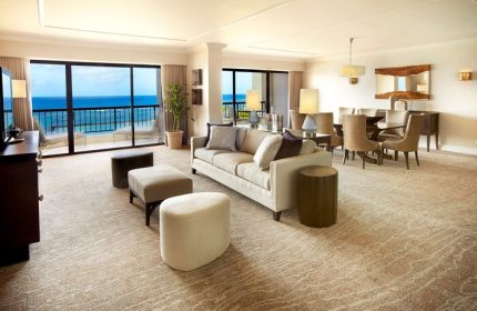 Hilton Hawaiian Village suite interior. Waikiki Beach Resort gay-friendly hotel room with ocean view, living area, dining table, and neutral decor.