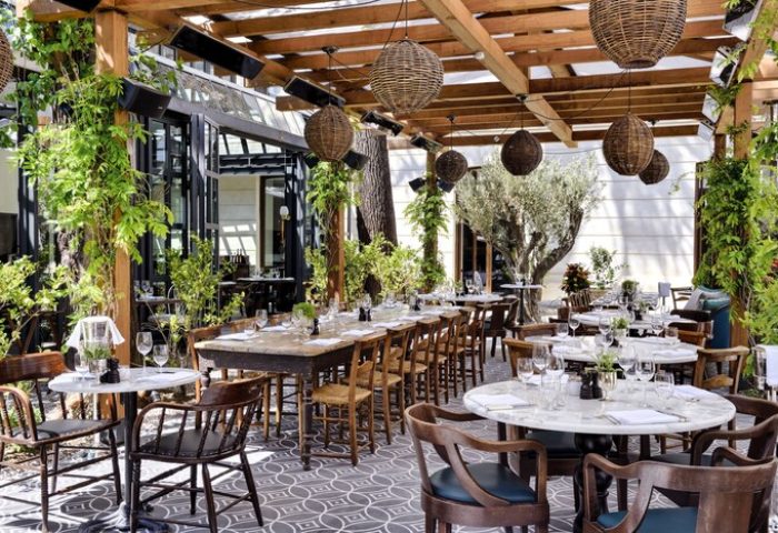 Soho House Istanbul's gay-friendly hotel outdoor dining area. Tables, chairs, plants, and decorative lighting create an inviting atmosphere.