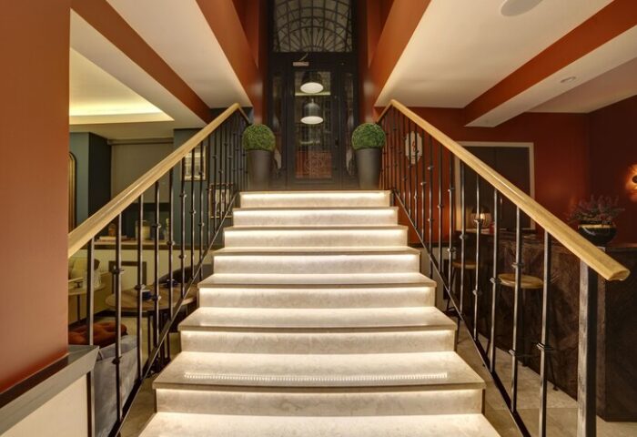 Staircase at The Fox Hotel, a gay-friendly hotel. Interior view of stairs with railings, leading to a glass door. Modern design, warm lighting.