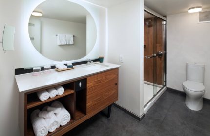 The Laylow Autograph Collection gay-friendly hotel bathroom. Modern design with round mirror, vanity, shower, and toilet. Great for gay men travel.