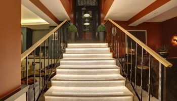 Staircase at The Fox Hotel, a gay-friendly hotel. Interior view of stairs with railings, leading to a glass door. Modern design, warm lighting.