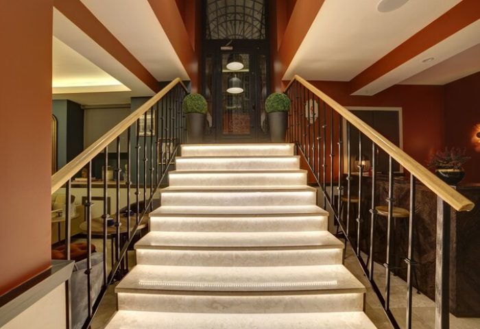 Staircase at The Fox Hotel, a gay-friendly hotel. Interior view of stairs with railings, leading to a glass door. Modern design, warm lighting.