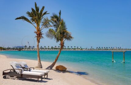W Dubai - Mina Seyahi gay-friendly hotel beach view. Palm trees, lounge chairs, and turquoise water create a relaxing scene for gay travelers.