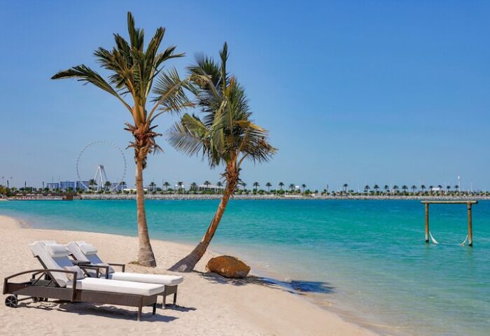W Dubai - Mina Seyahi gay-friendly hotel beach view. Palm trees, lounge chairs, and turquoise water create a relaxing scene for gay travelers.
