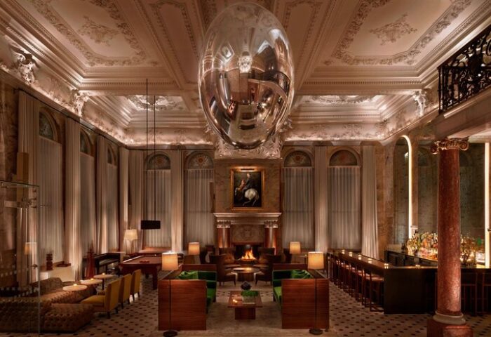The London EDITION hotel interior. A gay-friendly hotel with a bar, fireplace, pool table, and a large silver egg-shaped ornament hanging from the ceiling.