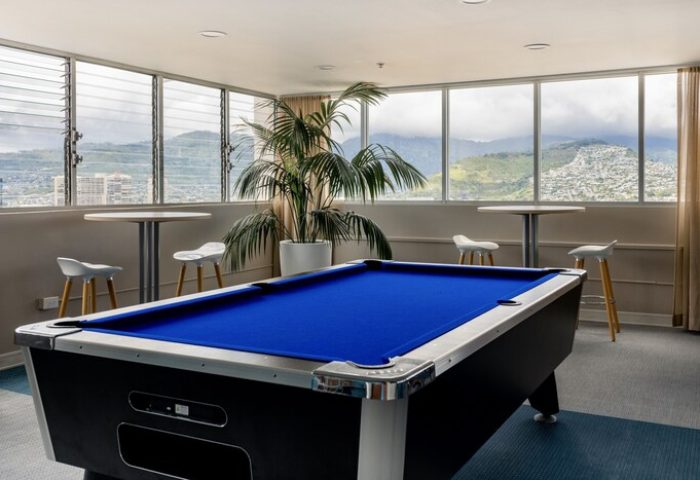 Pacific Monarch Hotel's game room with a blue pool table, high top tables, and views of Honolulu. This is a gay-friendly hotel.