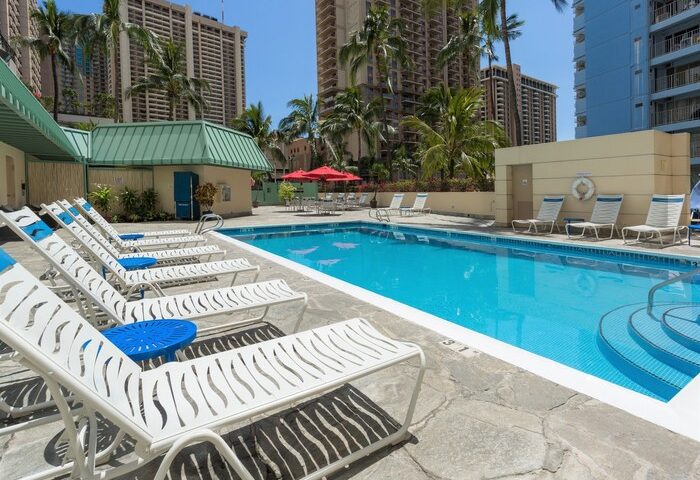 Ramada Plaza by Wyndham Waikiki pool area. Gay-friendly hotel with lounge chairs, umbrellas, and palm trees. Great for gay travel in Honolulu.