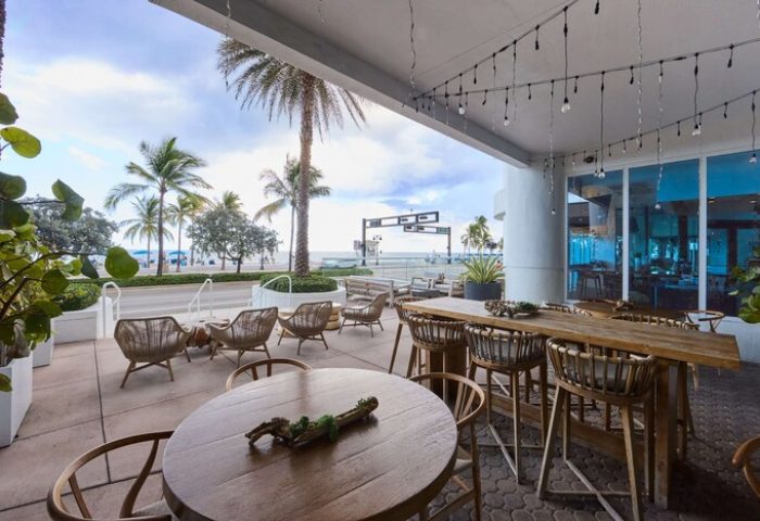 Outdoor dining at the gay-friendly Hilton Fort Lauderdale Beach Resort. Tables and chairs offer a view of the beach. Palm trees.