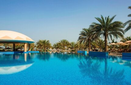 Le Royal Méridien Beach Resort & Spa pool view. Gay-friendly hotel with palm trees, blue water, and a clear sky. Perfect for gay travel.