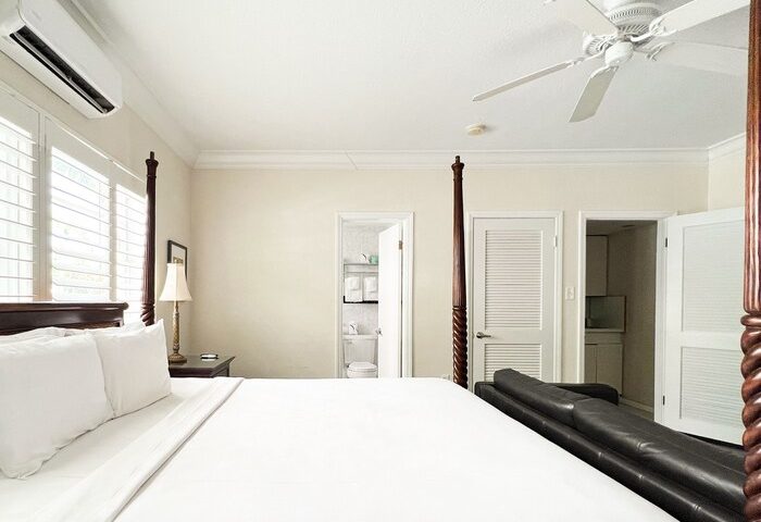 La Casa Hotel gay-friendly room. Four-poster bed with white linens, ceiling fan, and bathroom access. Ideal gay travel lodging.