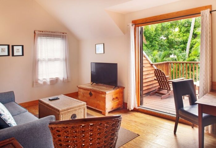 Island City House gay-friendly hotel room. Living area with balcony, chair, TV, and couch. Perfect for gay travelers seeking comfort and style.