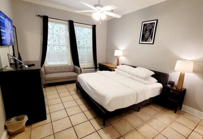 Equator Resort gay-friendly hotel room. King bed with white linens, sofa, TV, ceiling fan, lamps, and black and white art. Key West gay travel.