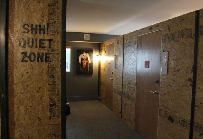 Hallway at Gaythering, a gay-friendly hotel. Crates form walls with SHH! Quiet Zone sign. An art piece adds to the hotel's ambiance.