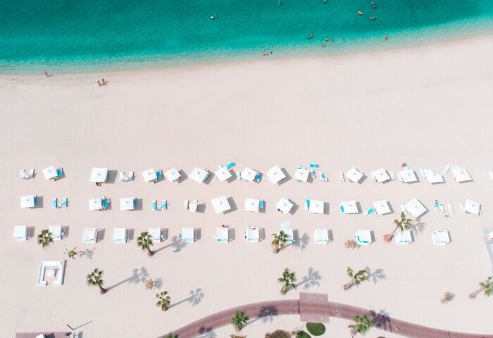 Aerial view of Nikki Beach Resort & Spa Dubai, a gay-friendly hotel. White beach, turquoise water, sunbeds, and palm trees. Ideal for gay travel.