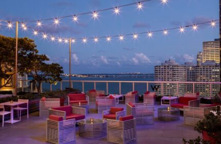W Miami gay-friendly hotel rooftop lounge at dusk. String lights illuminate outdoor seating with city and ocean views. Perfect for gay travel.