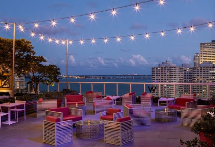 W Miami gay-friendly hotel rooftop lounge at dusk. String lights illuminate outdoor seating with city and ocean views. Perfect for gay travel.