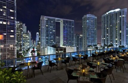 Kimpton EPIC Hotel's rooftop restaurant at night. Gay-friendly hotel with stunning city views. Miami skyline with illuminated skyscrapers.