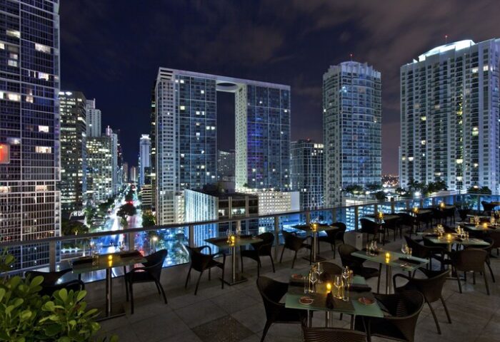 Kimpton EPIC Hotel's rooftop restaurant at night. Gay-friendly hotel with stunning city views. Miami skyline with illuminated skyscrapers.