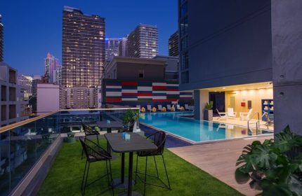 Hotel Indigo Miami Brickell gay-friendly hotel rooftop pool at night. Tables, chairs, city skyline. Modern design.