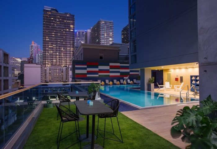 Hotel Indigo Miami Brickell gay-friendly hotel rooftop pool at night. Tables, chairs, city skyline. Modern design.